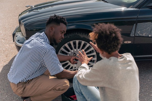 A man and a woman crouch next to the wheel of a car.